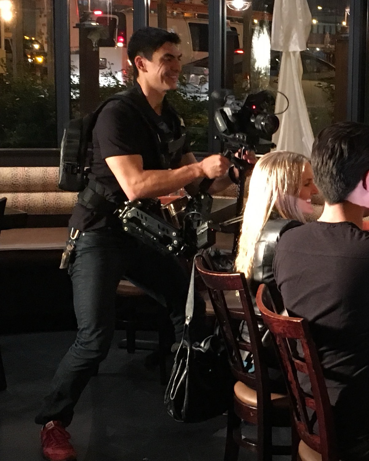 Scott Williams operating a Steadicam rig on a restaurant set at night, camera balanced in front of him, smiling as he lines up the shot.